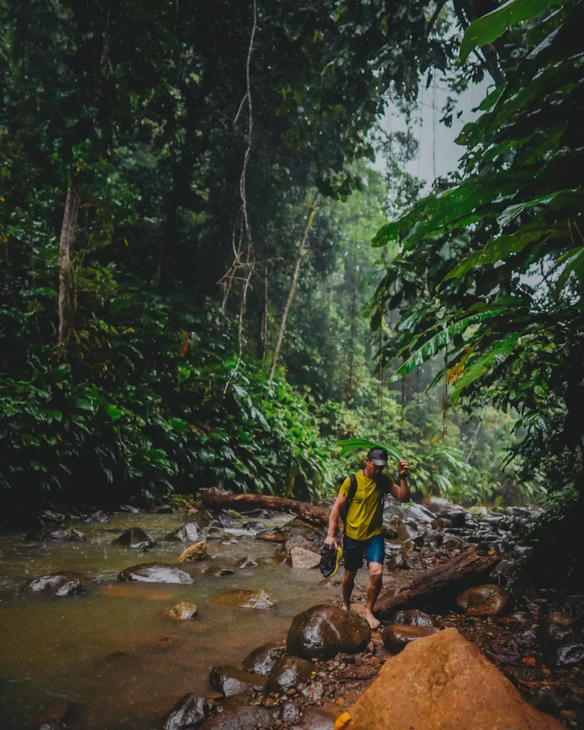Randonneur marchant sur les galets de la Ravine Tambour sous la pluie en Guadeloupe.

