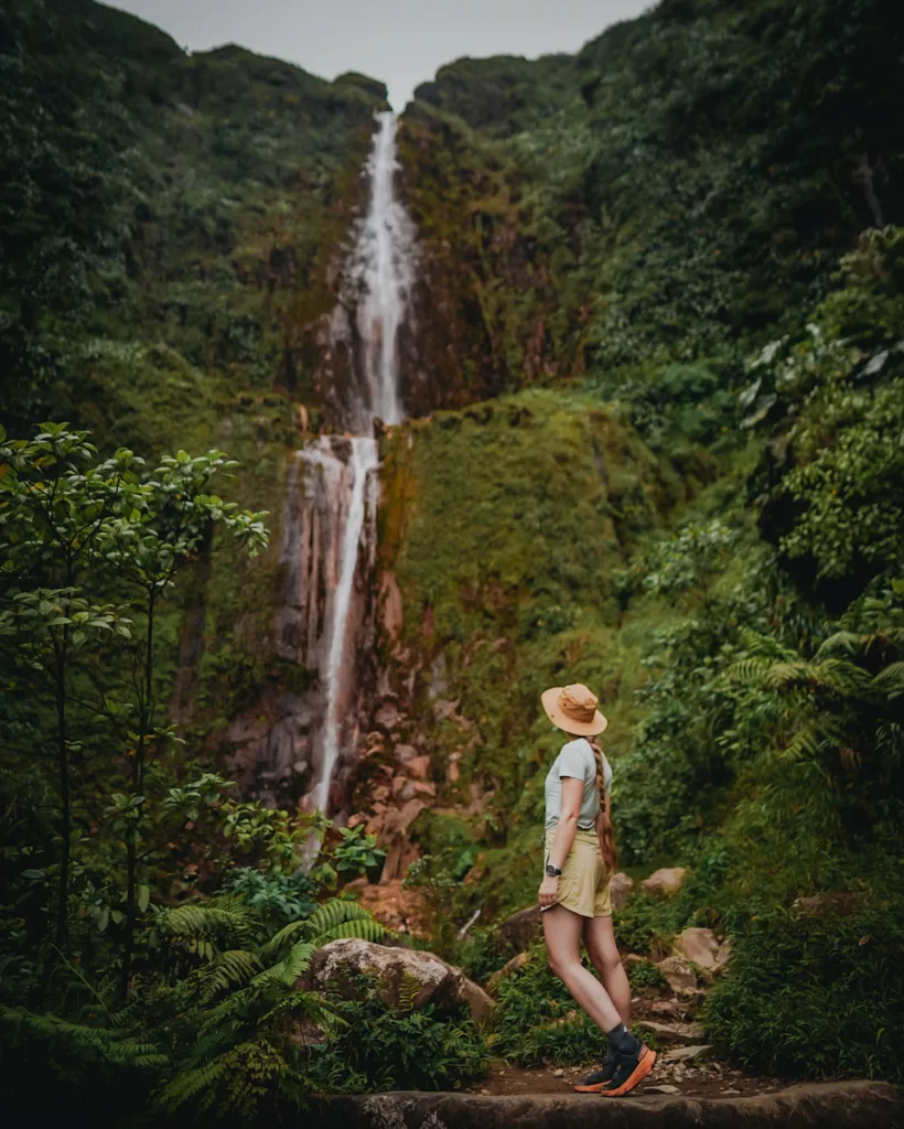 Portrait de randonneuse admirant la chute du Carbet en arrière-plan, au cœur de la forêt guadeloupéenne.

