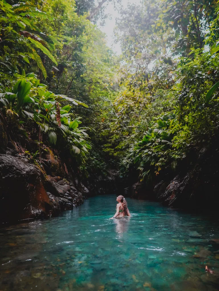 Femme marchant dans l’eau claire au fond du canyon de la rivière Moustique, en pleine nature guadeloupéenne.

