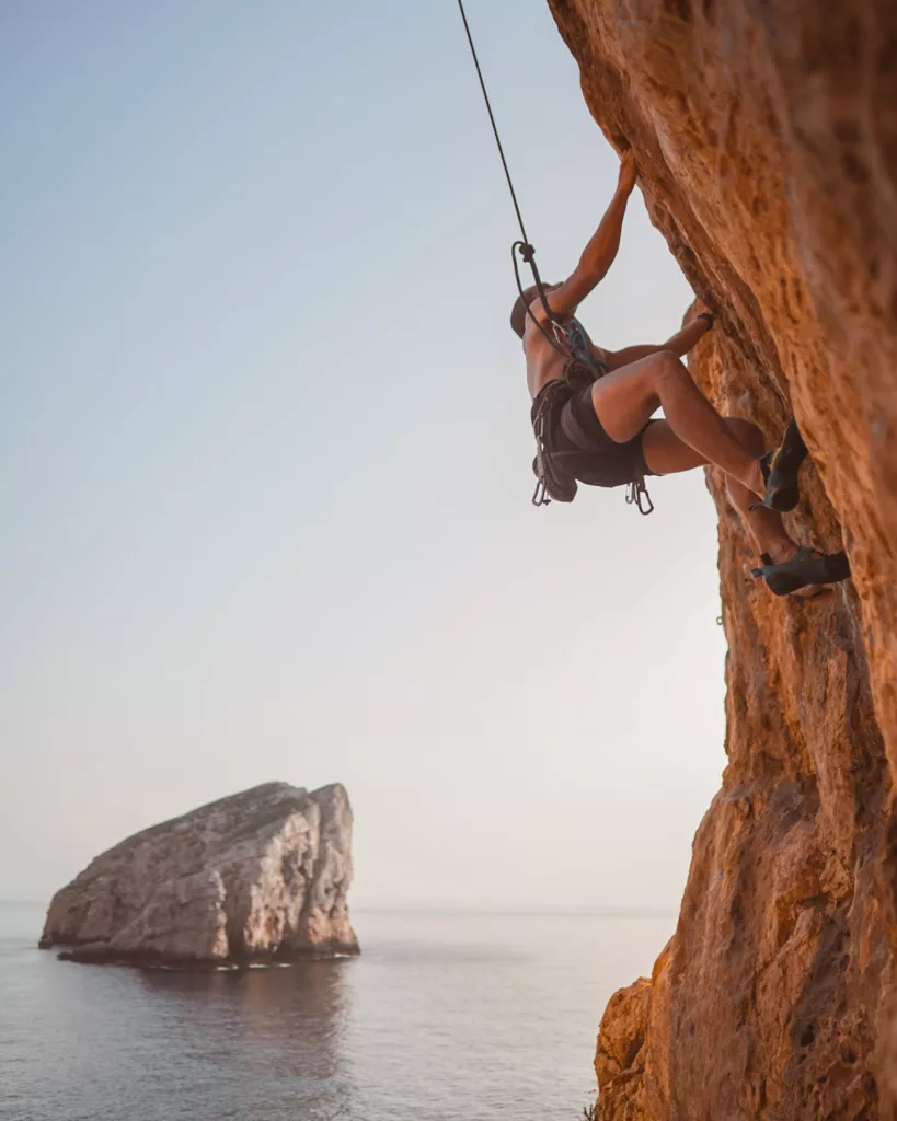 Grimpeur qui fait de l'escalade sur une falaise orange surplombante au-dessus de la mer méditerranée à Capo Caccia en Sardaigne.