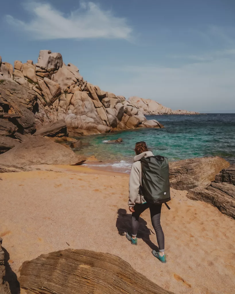 Femme qui marche sur la plage de sable doré à Capo testa en direction des rochers d'escalade de granit orangés.