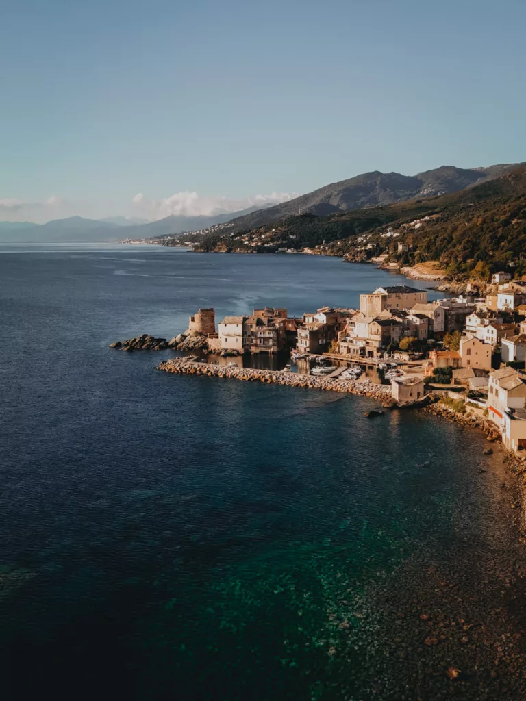Erbalunga, village de pêcheur dans le Cap Corse, visite de la Haute-Corse, guide complet des plus beaux villages en Corse. Vue de la tour génoise d'Erbalunga et des montagnes du Cap Corse avec Bastia en arrière-plan.