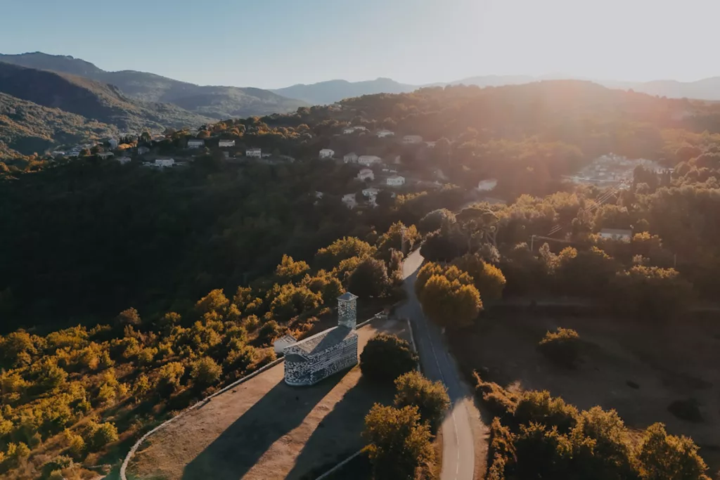Eglise San Michele de Murato en Corse vue du ciel en drone avec le village de Murato en arrière-plan au coucher du soleil.