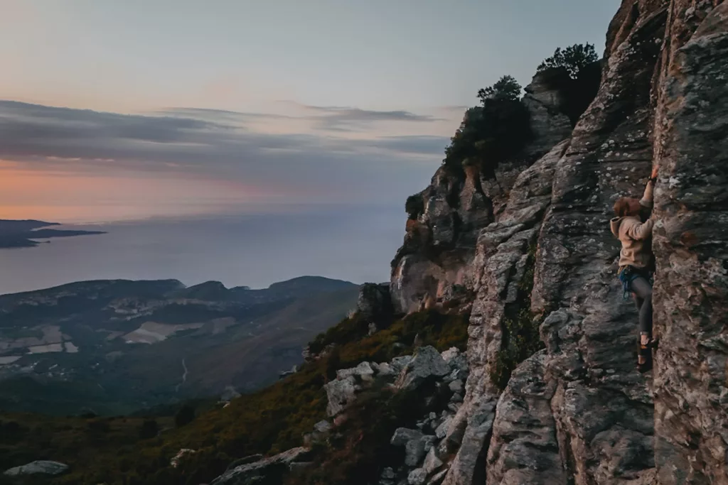 Escalade en Corse au coucher du soleil secteur des antennes dans le Cap Corse proche de Bastia et Saint-Florent. Jeune femme qui grimpe sur la falaise.