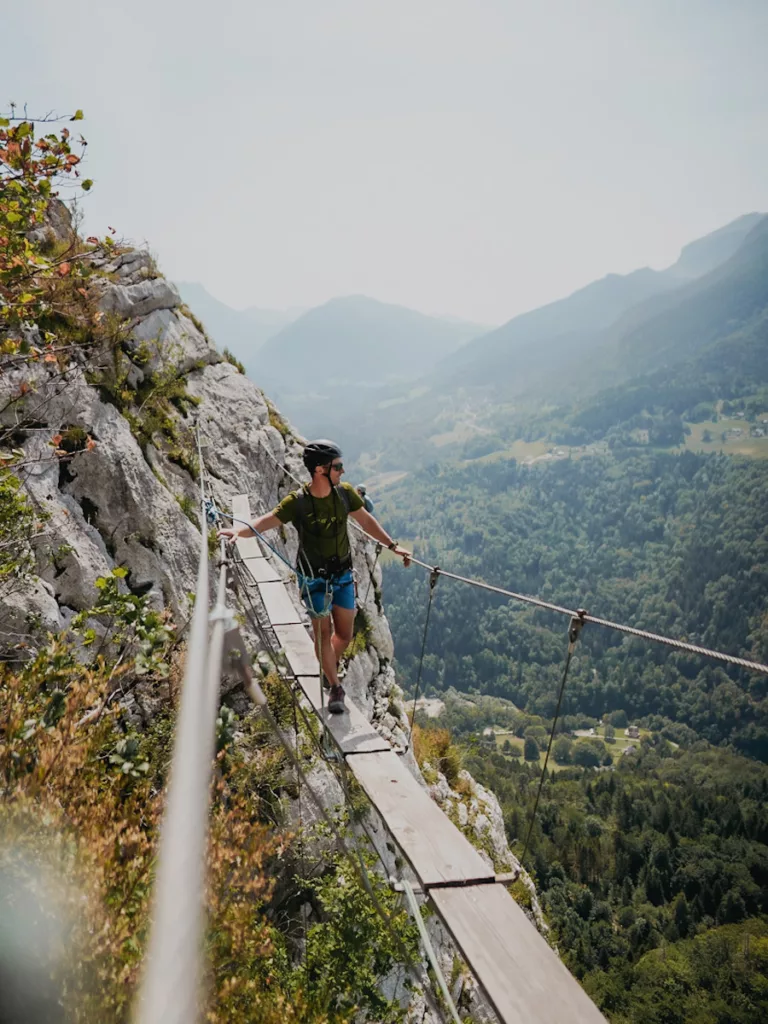 Homme qui marche sur un pont suspendu sur Via Ferrata de la Roche Veyrand à Saint Pierre d'Entremont en Savoie.