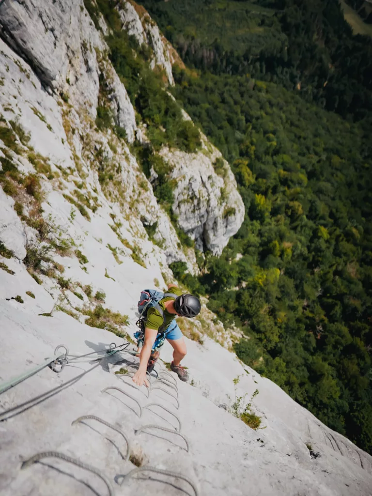 Homme qui grimpe sur une échelle de Via Ferrata face au vide au-dessus de la forêt. Via Ferrata de la Roche Veyrand à Saint Pierre d'Entremont en Savoie.