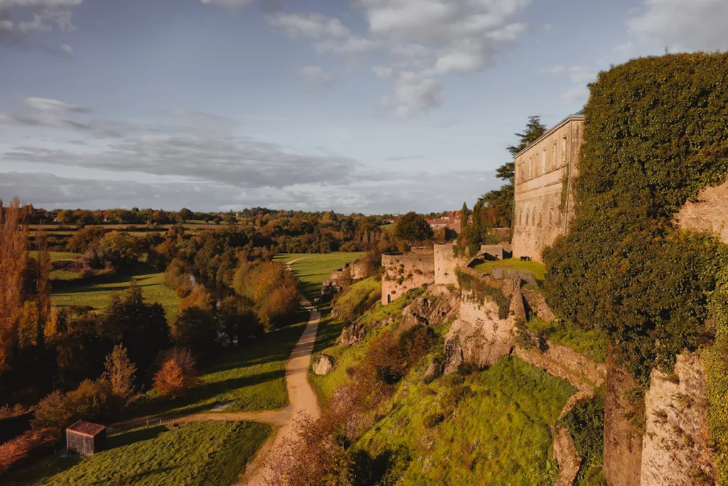 Vue des remparts de la cité médiévale de Parthenay depuis le bord de la rivière Thouet, lors d’une visite, avec les murs de pierre dominants la rive et reflétant l’histoire de la ville.