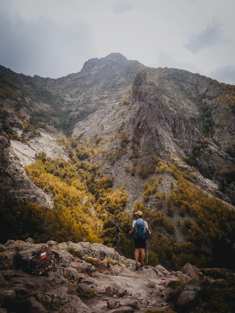 GR20 en automne, homm qui marche sur le sentier du GR20 façe aux montagnes corses.