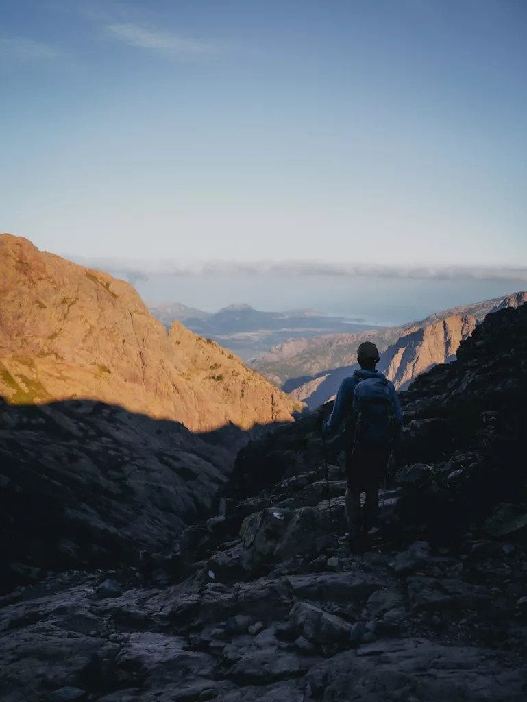 Homme (randonneur) qui contemple le paysage au mever du soleil, vue sur la baie de Calvi et les montagnes en Corse.