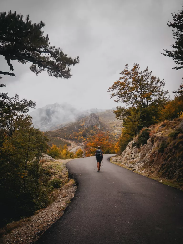 Randonneur marchant sur une route proche de Ghisoni sur le GR20 en automne par temps brumeux.