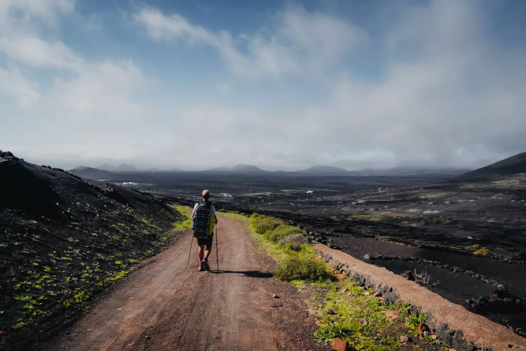 Randonneur sur le GR131 à Lanzarote, passage au milieu des vigne de la Geria. Itinéraire de trek sur les îles Canaries.
